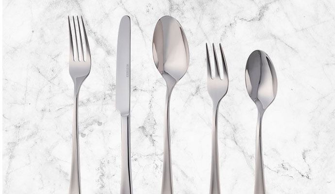 Meisterkoch-gelabeltes Besteckset aus Edelstahl vor weißem Marmor, konkret: Gabel, Messer, Löffel, Kuchengabel, Teelöffel