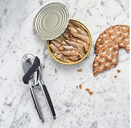 Dosenöffner, geöffnete Dose mit Anchovis und Knäckebrot - im Hintergrund weißer Marmor
