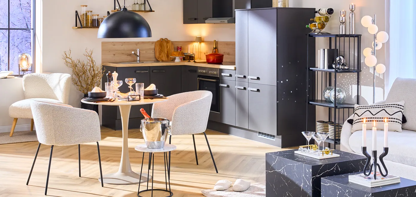 Eck-Einbauküche in Dunkelgrau, dazu kleiner runder Esstisch in Kaschmirfarben und grauen Stoffstühlen, kleiner Beistelltisch mit Sektkühler und gedecktem Tisch, Marmor-Couchtische in Schwarz, Diskokugeln und Chromdeko