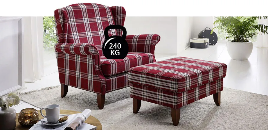 Wohnzimmer mit Ohrensessel und Hocker in rotem, karierten Bezug. Kleines Hantelsymbol auf der Sitzfläche mit Beschriftung 240 kg.