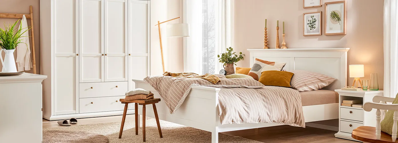 Schlafzimmer mit weißen Landhaus-Möbeln der Chester Serie: Kleiderschrank mit 4 Türen und 2 Schubladen, Nachttisch. Dazu ein weißes Doppelbett.