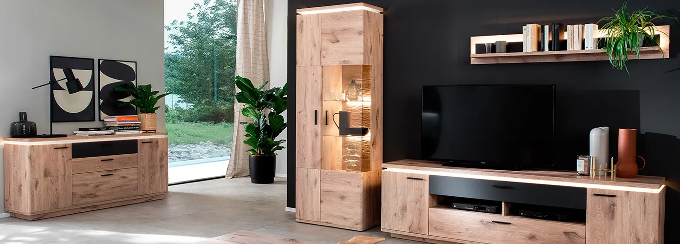 Wohnzimmer mit Möbeln in Holzoptik, bestehend aus Sideboard, Vitrine, Wandboard und Lowboard, alle mit LED-Oberbodenbeleuchtung, Sideboard, Wandboard und Lowboard mit Akzenten in Anthrazit, Deko
