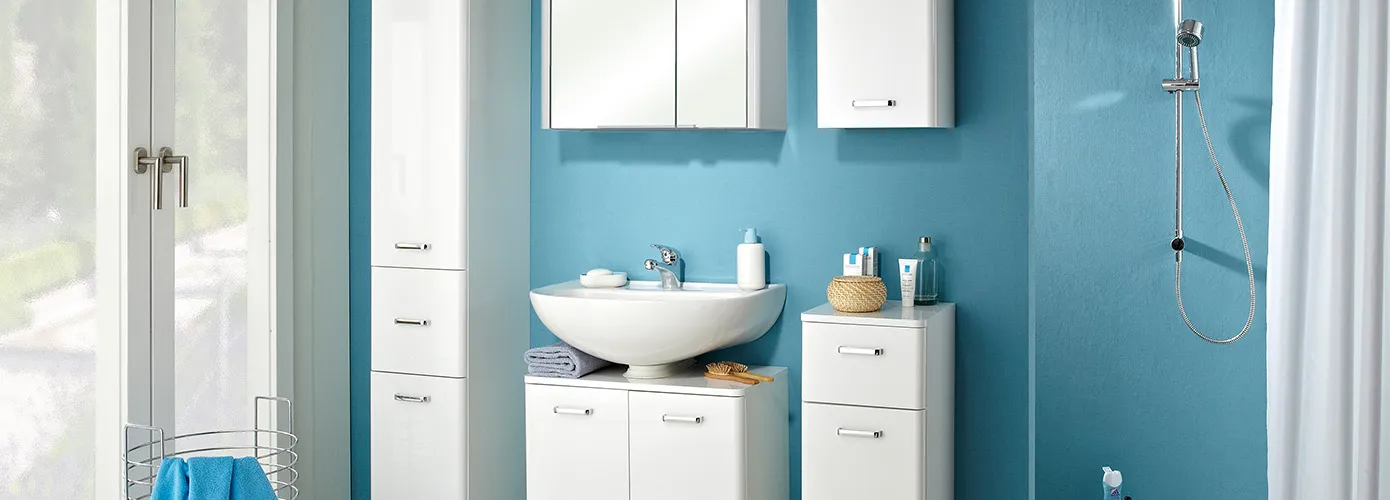Badezimmer mit weißen Badmöbeln, bestehend aus Hochschrank, Spiegelschrank, Waschbeckenunterschrank, Hängeschrank und Unterschrank, Fenster und Dusche, blaue Wände, weißer Duschvorhang