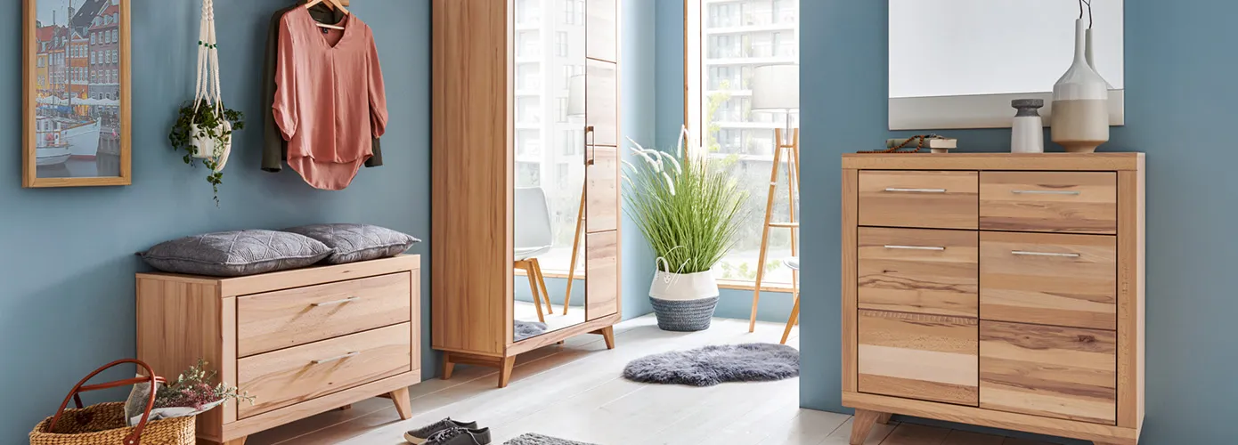 Flur mit Flurmöbeln aus Holz im Skandi-Stil, bestehend aus Gardeobenbank mit grauen Kissen, Garderobenschrank mit einer Spiegeltür, Kommode und Spiegel, Kleidung, Deko.