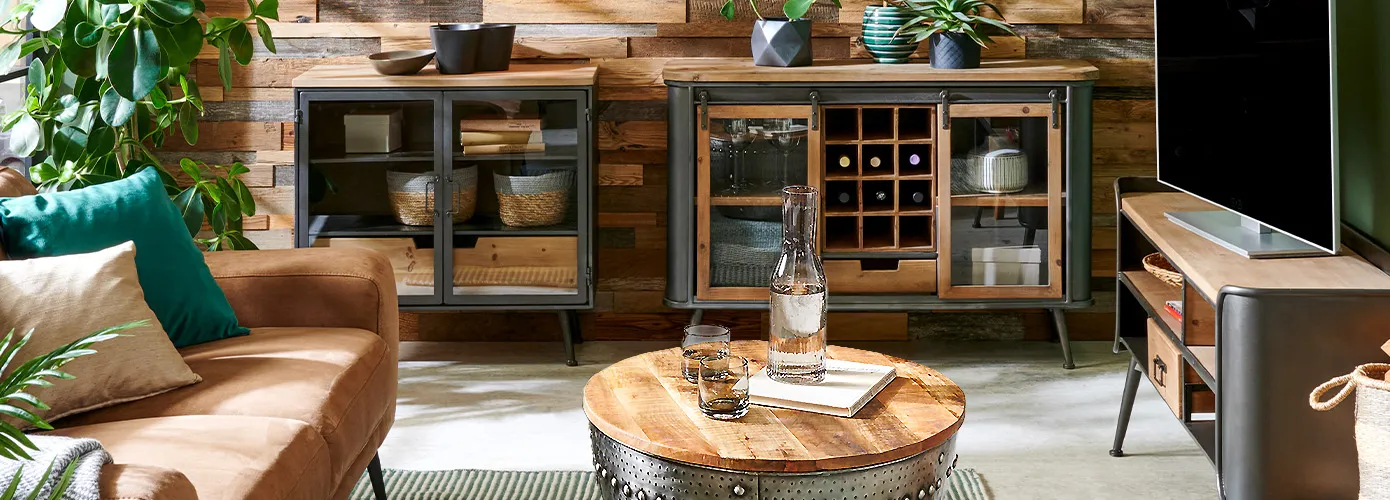 Industrial-Wohnzimmer mit braunem Sofa, 2 Kommoden und einem Lowboard in Holzoptik und grauem Metall, runder Couchtisch mit Holztischplatte und Metallgestell mit Nieten