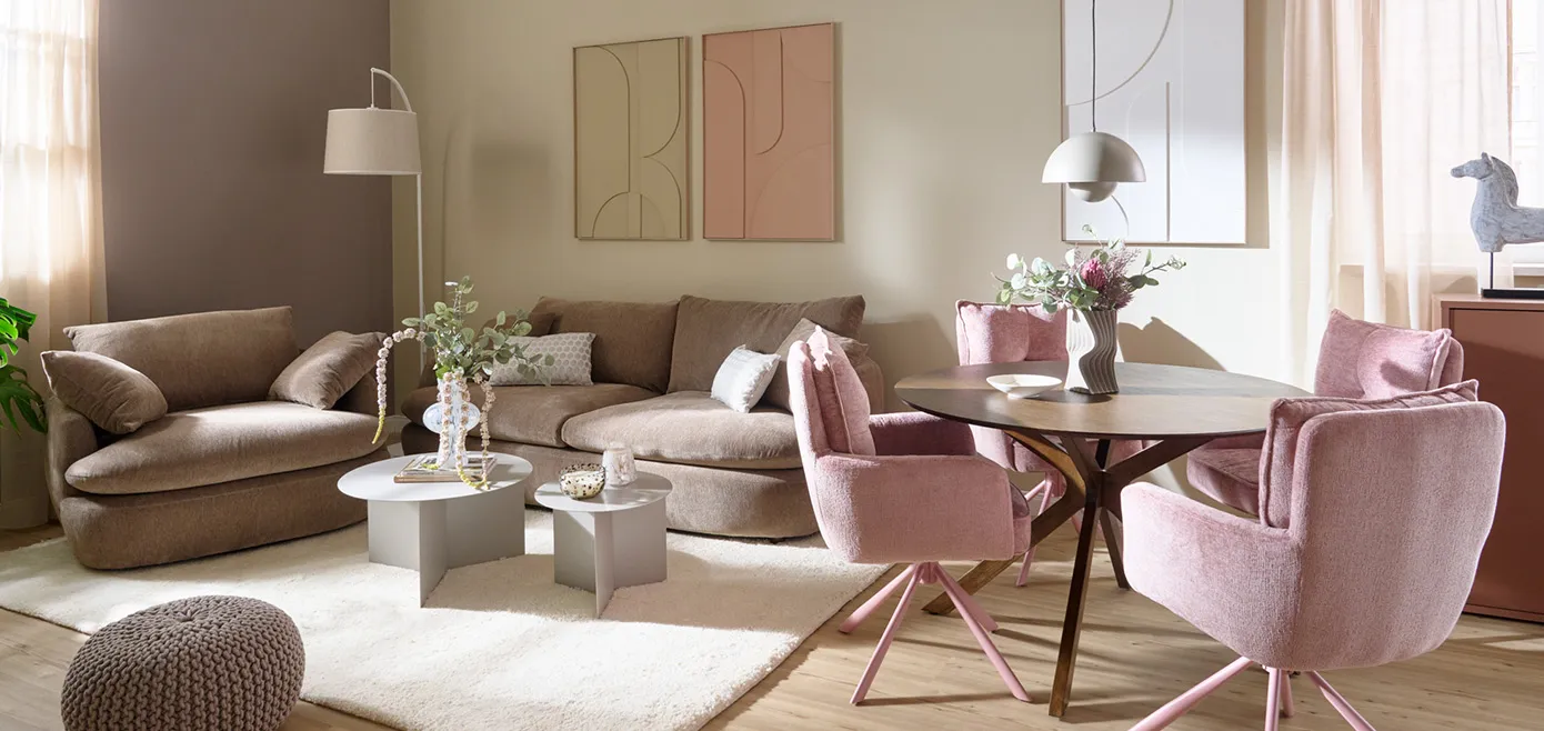 Wohnzimmer mit taupe Sessel und Big Sofa in runden Formen, weißer Teppich, zwei graue Couchtische rund, runder Esstisch aus dunklem Holz und vier rosa Polsterstühlen