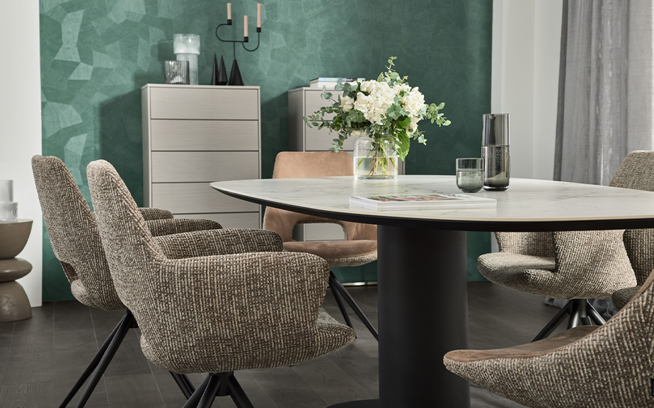 Esszimmer mit Säulentisch mit schwarzer Säule und Tischplatte in weißer Marmoroptik, Polsterstühle mit beige-meliertem Bezug, cremefarbige Highboards, Deko