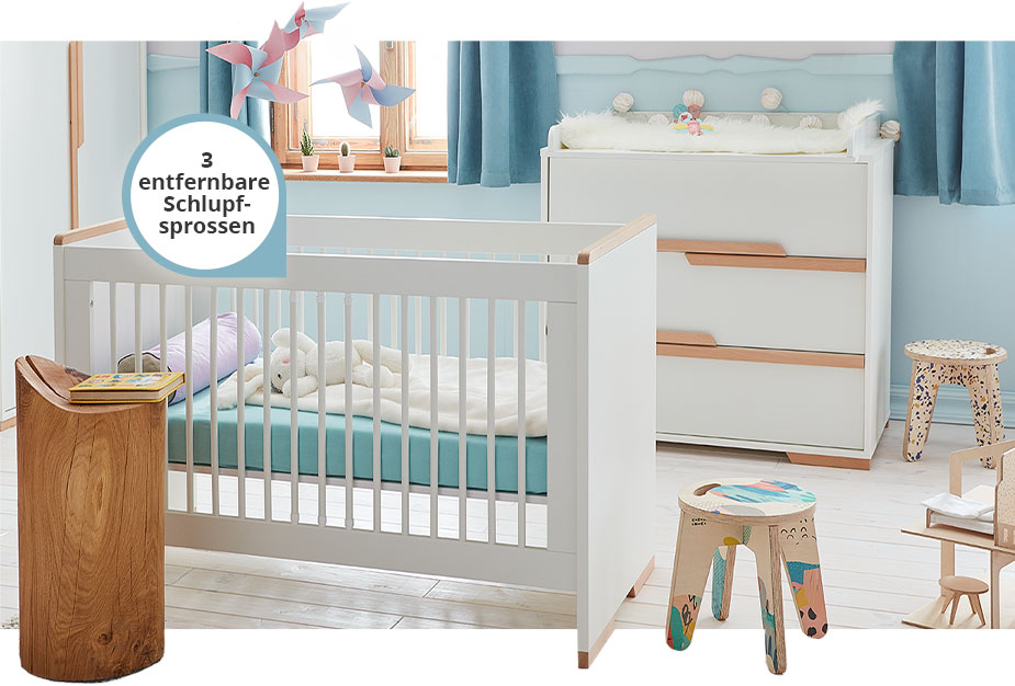 Babyzimmer mit Kleiderschrank, einem Babybett, einer Wickelkommode mit Wickelaufsatz, Hinweis am Babybett: "3 entfernbare Schlupfsprossen", Möbel weiß mit Holzakzenten