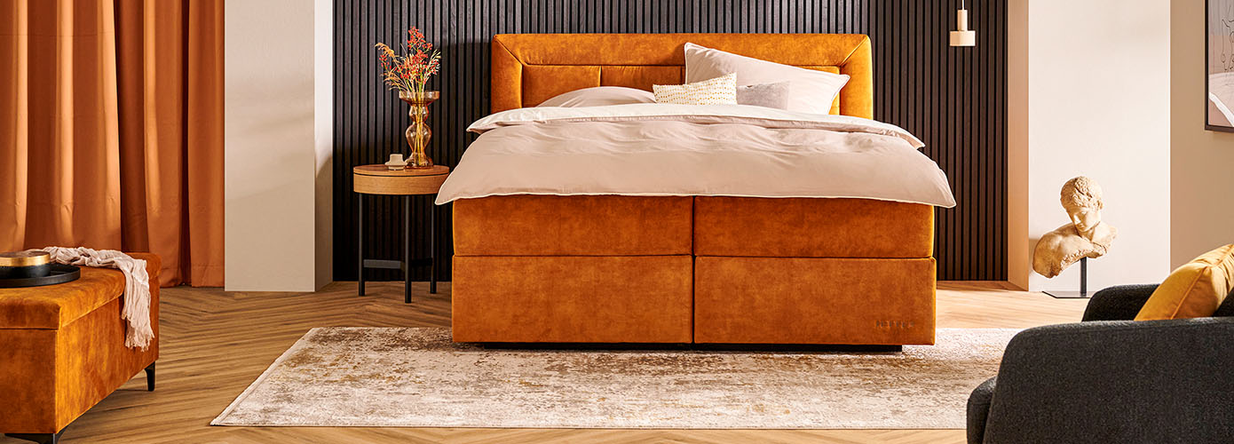 Schlafzimmer mit kupferfarbenem Boxspringbett und Teppich im Vintage-Design in Beige und Braun