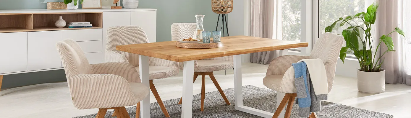 Esszimmer mit Esstisch aus Holz mit U-Gestell aus weißem Metall, 4 Polstersessel aus beigem Cord mit Holzgestell, grauer Teppich, weißes Sideboard, Deko. 
