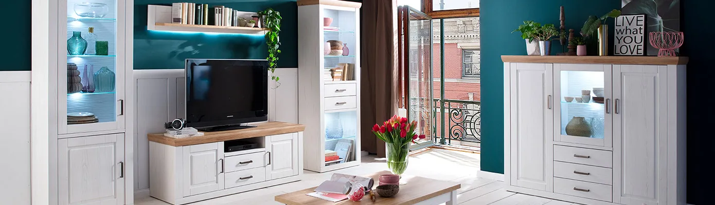 Wohnzimmer mit weißen Landhausmöbeln und Holzakzenten, bestehend aus 2 Vitrinen, Lowboard, Wandboard und Couchtisch. Vitrinen mit Beleuchtung, Deko.