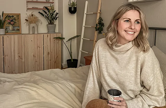 Frau auf beigem Bett, Holzkommode, Deko
