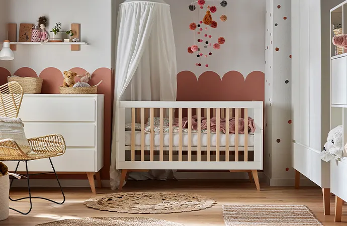 Babyzimmer im Skandi-Stil mit weißen Möbeln mit Holzakzenten, bestehend aus Kommode, Wandregal, Babybett mit Hikmmel, Schrank und Regal, Rattan-Sessel, Deko