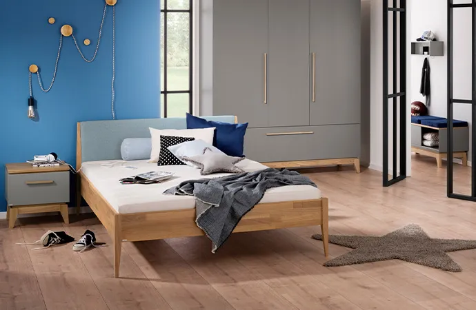 Jugendzimmer im Skandistil mit grauen Möbeln mit Holzakzenten, bestehend aus Nachtkommode, Bettgestell, Schrank, grauer Teppich in Sternform, Deko.