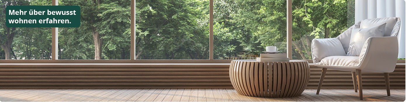 Mehr über bewusst wohnen erfahren. Sessel und Couchtisch vor Fensterfront, dahinter ein Wald