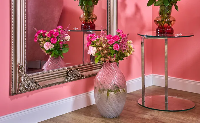 Großer Wandspiegel in Stuckoptik, Glas-Beistelltisch und rosane Vase