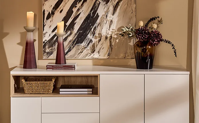 Weiße Kommode vor Beiger Wand mit Kerzenständern und Vase