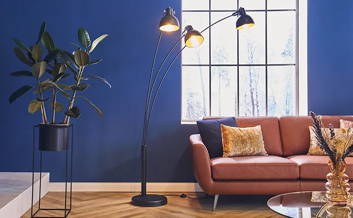 Braunes Ledersofa mit goldenen und blauen Dekokissen, schwarze Stehlampe mit drei Leuchten