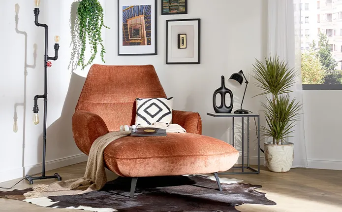 Brauner Sessel mit Tierfell-Teppich, Kissen mit Rautenmuster, schwarze rustikale Stehlampe und schwarze Deko