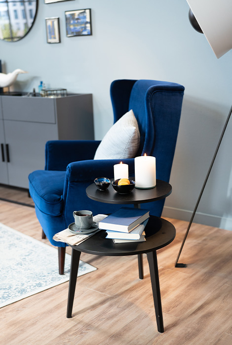 Royalblauer Samtsessel mit zwei schwarzen, runden Beistelltischen