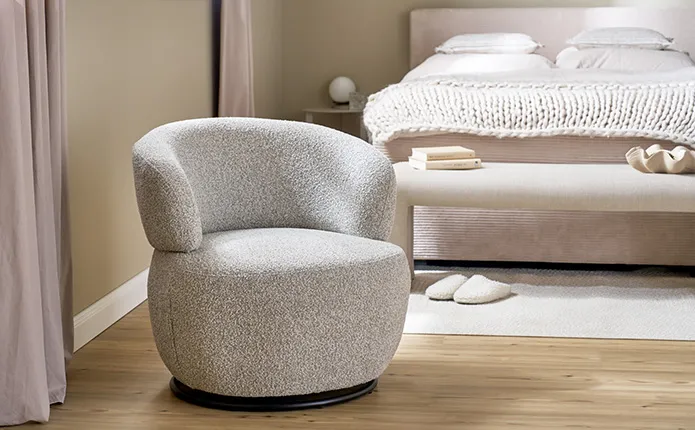 Runder, hellgrauer Drehsessel gepolstert, im Hintergrund beiges Cordbett und beige Sitzbank