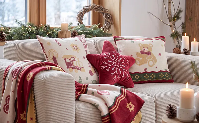 beiges Cordsofa mit Dekokissen und Decke mit traditionellen Weihnachtsmustern in rot, grün, creme