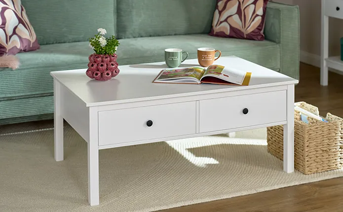 Nahaufnahme weißer, rechteckiger Couchtisch im Landhausstil mit zwei Schubladen und schwarzen Knaufen, darauf Himbeervase zur Deko und zwei Tassen in braun und grün