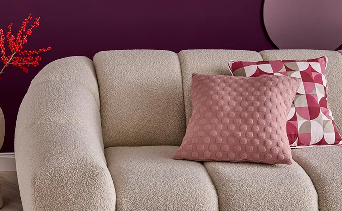 Detailansicht Sofa in Creme und Boucléstoff, Dekokissen in Rosa mit erhabenen Punkten als Muster, weiteres Dekokissen passend zur Bettwäsche in verschiedenen Beerentönen und runden Mustern