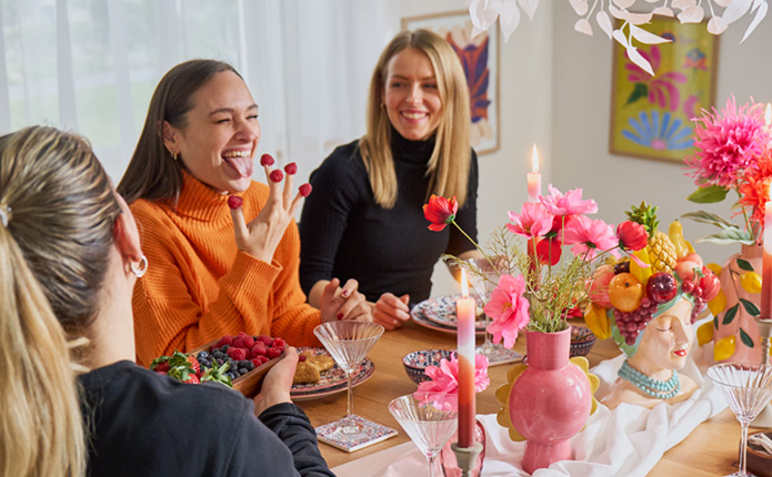 Drei Freundinnen am gedeckten Tisch und bunter Dekoration mit vielen Blumen haben Spaß