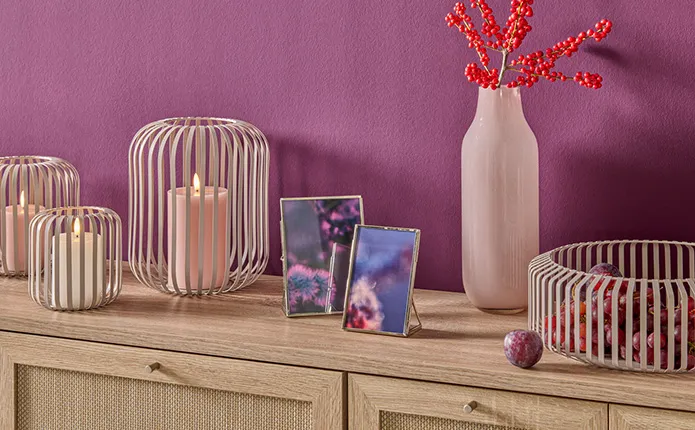 Detailansicht Holzkommode mit kaschmirfarbenen Windlichtern in Lamellenoptik, Bilderrahmen mit Dekobildern in Beerentönen, Lila Wand