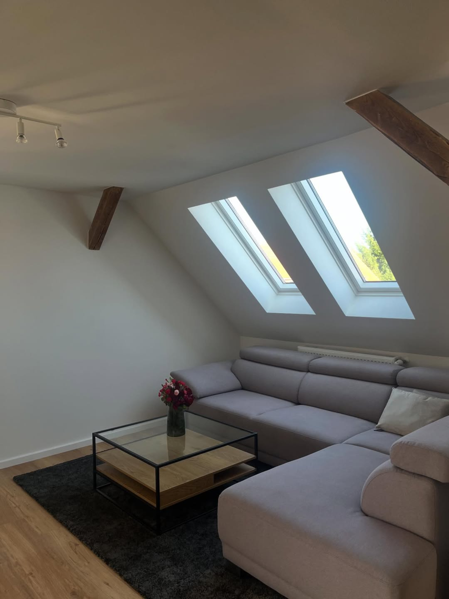 Hellgraues Ecksofa mit Dachschräge, quadratischer Holz-Couchtisch mit Glasplatte und Blumenstrauß