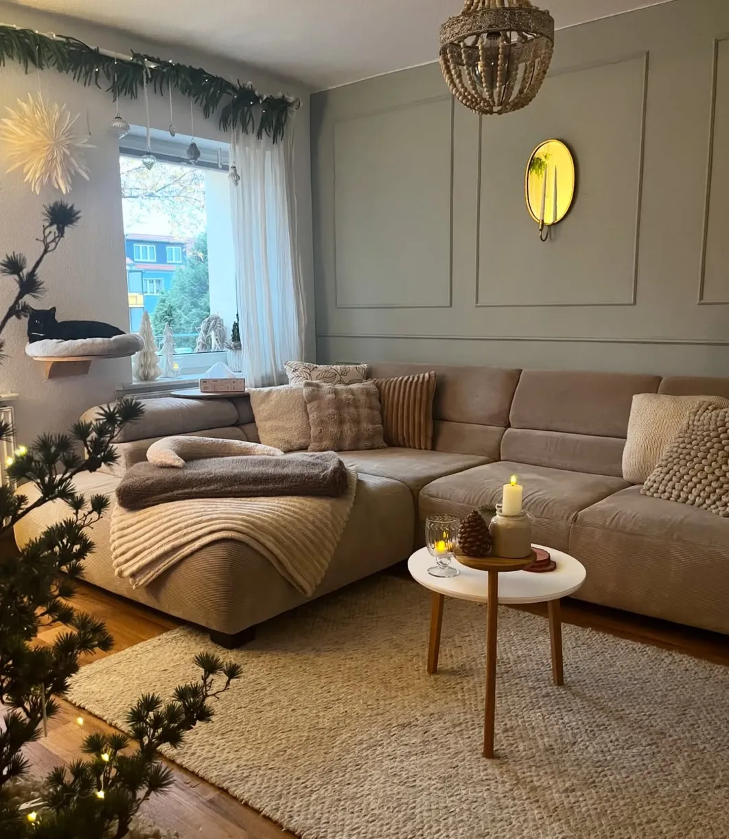 Hellgraues Ecksofa aus Cord mit dunklem Holzboden und schwarzen Accessoires wie Regal und Pendelleuchte