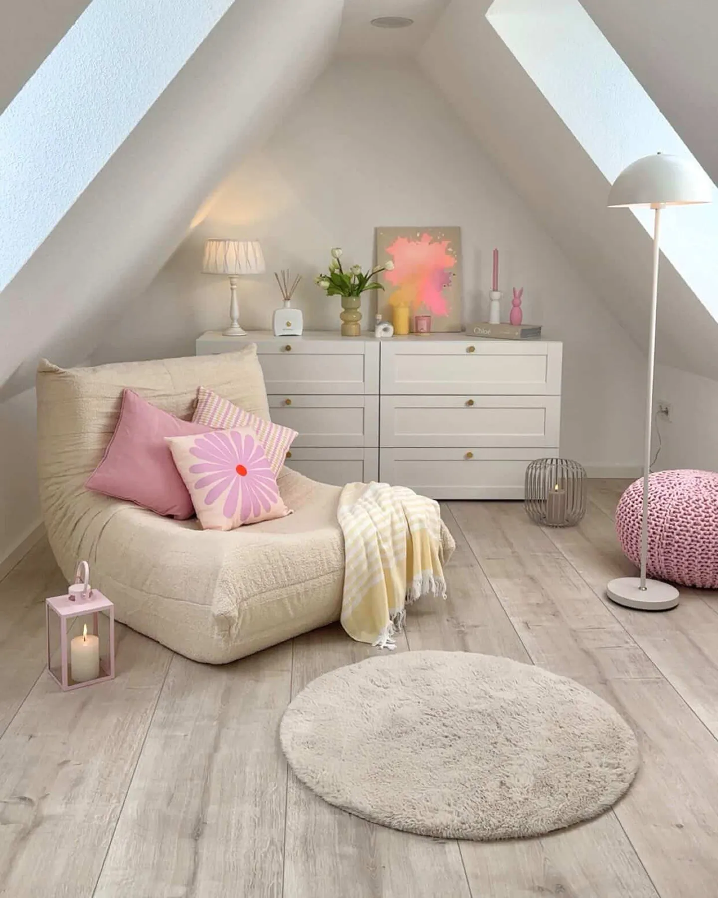 Runde rosa Glasvase mit Frühlingsblumen auf Holz-Couchtisch, dahinter grau-beiges Sofa mit beigen Kissen und Rautenmuster