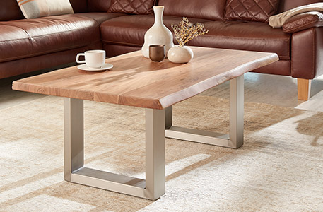 Couchtisch mit Massivholztischplatte und U-Kufengestell in Edelstahloptik vor braunem Eck-Ledersofa