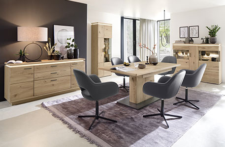 Esszimmer mit Essgruppe bestehend aus Holz-Esstisch und grauen Polsterstühlen mit schwarzem Drehgestell - im Hintergrund Stauraummöbel aus Holz