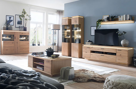 Wohnzimmer mit grauer Couch und Wohndecke im Vordergrund - Couchtisch, Highboard und Wohnkombination im Holzdekor