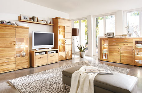 Wohnzimmer mit Lederhocker in Grau im Vordergrund - Wohnkombination und Highboard im Holzdekor im Hintergrund