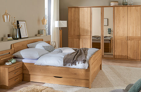 Schlafzimmer mit Bett, Nachtkommode und Schrank aus Holz mit zwei Schranktüren aus Spiegel