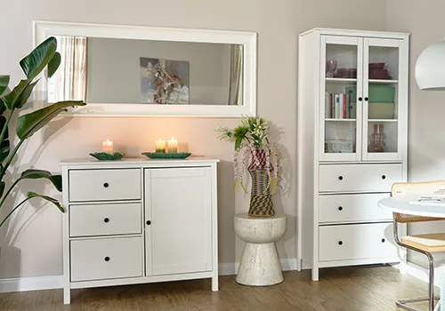 Schmaler, rechteckiger Spiegel mit weißen Rahmen an Wand in Horizonal über weißer Kommode, daneben weiße Vitrine