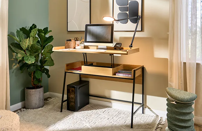 Ansicht Schreibtisch, Arbeitsplatte hochgefahren zum Arbeiten im Stehen mit Rechner, Bildschirm und Schreibtischlampe, beiger Bohoteppich