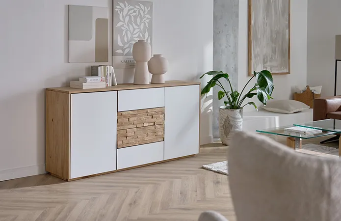 Ansicht weißes Sideboard mit Holzschubladen in der Mitte mit Steinvasen und Büchern, dahinter zwei künstlerische Dekobilder in Beigetönen, große Steinbodenvase mit großer Pflanze