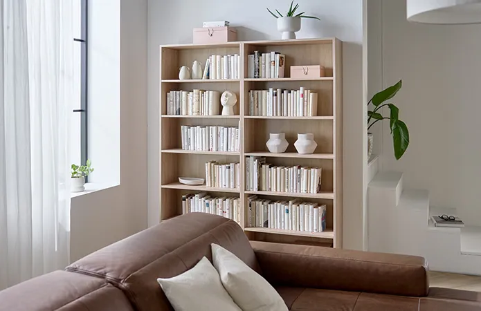 Ansicht von zwei hohen und hellen Holzregalen nebeneinander mit vielen Büchern und Dekovasen dazwischen