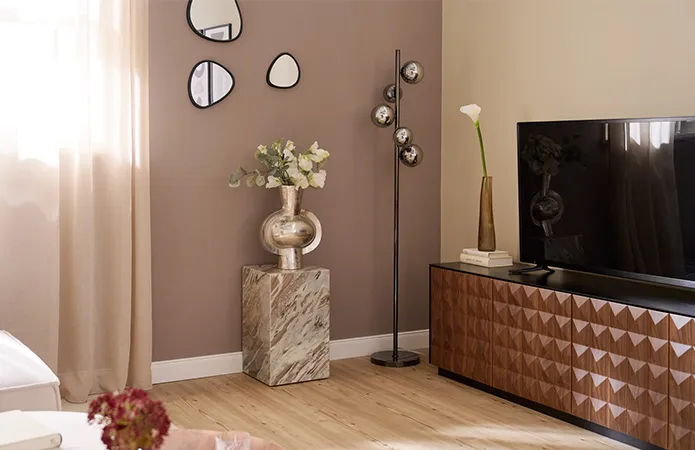 TV-Lowboard aus dunklem Holz, daneben Marmorcube mit großer Chromvase und weißen Blumen, drei organische Dekospiegel an Wand, Chrom-Stehleuchte