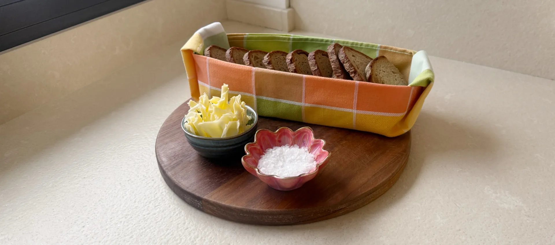 Geschirrtuch als Brotkorb mit Brot drin, angerichtet auf runder Holzplatte und kleinen Schälchen mit Butter und Salz