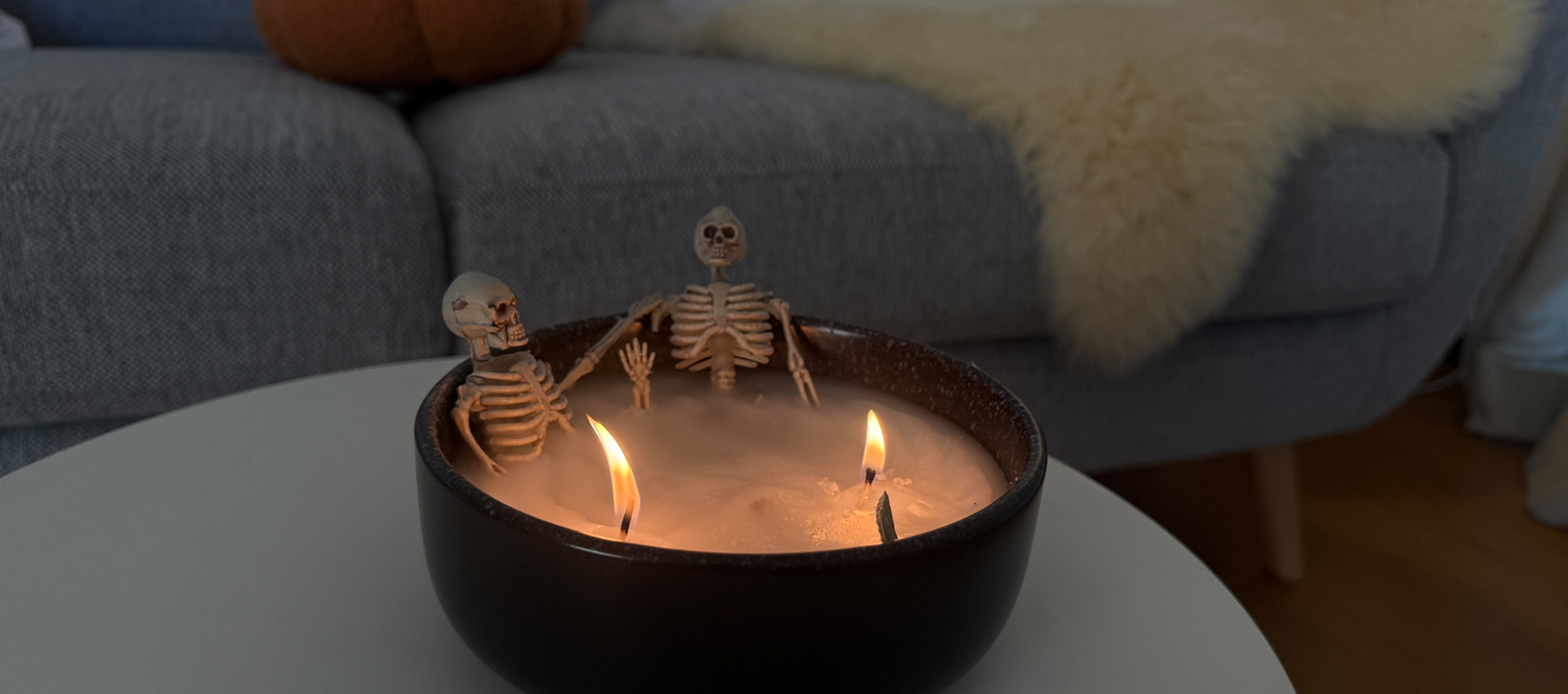 2 Skelette sitzen in einer schwarzen Schale aus Kerzenwachs wie in einer Badewanne mit 2 Dochten und angezündet als Kerze