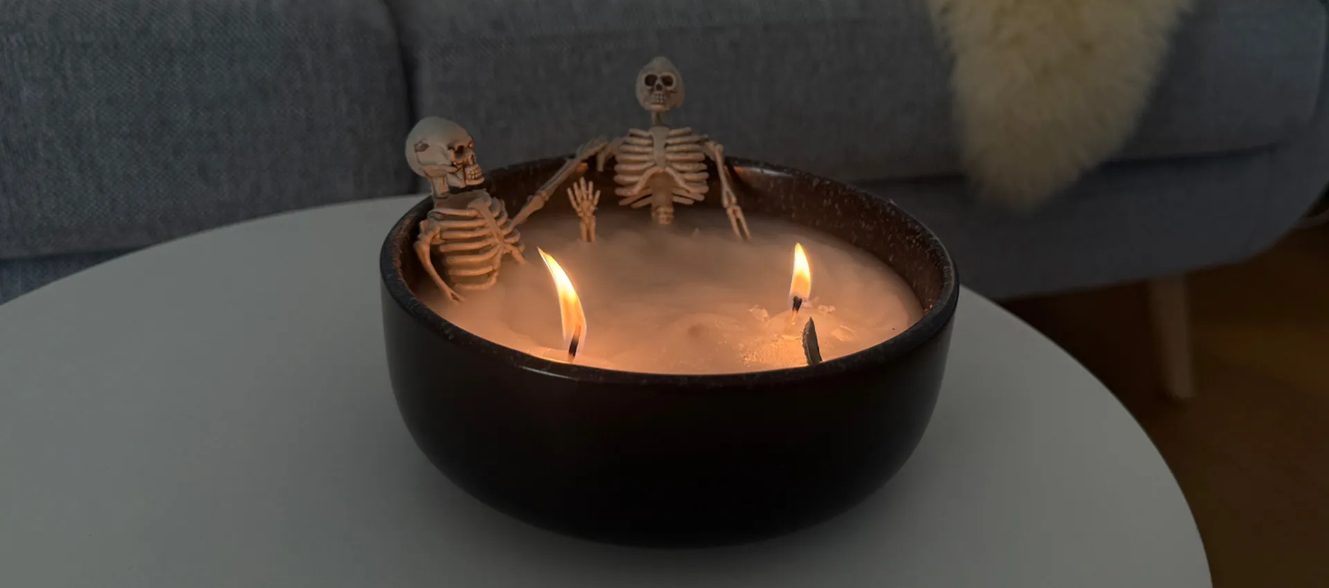 2 Skelette sitzen in einer schwarzen Schale aus Kerzenwachs wie in einer Badewanne mit 2 Dochten und angezündet als Kerze