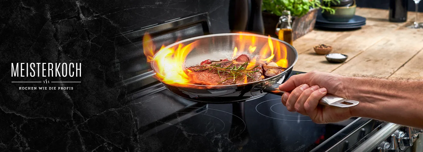 Meisterkoch, Kochen wie die Profis. Hand mit Bratpfanne, darin flambiertes Fleisch auf einem Herd.