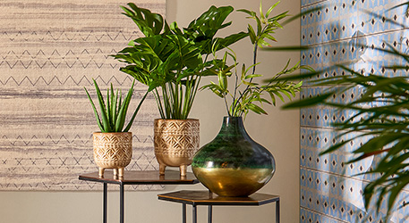 beige gemusterte Blumentöpfe mit Grünpflanzen und grün-goldene Vase mit Zweigen auf Beistelltischen
