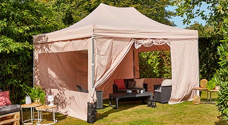 Pavillon in Beige, diverse Outdoormöbel, in einem Garten 