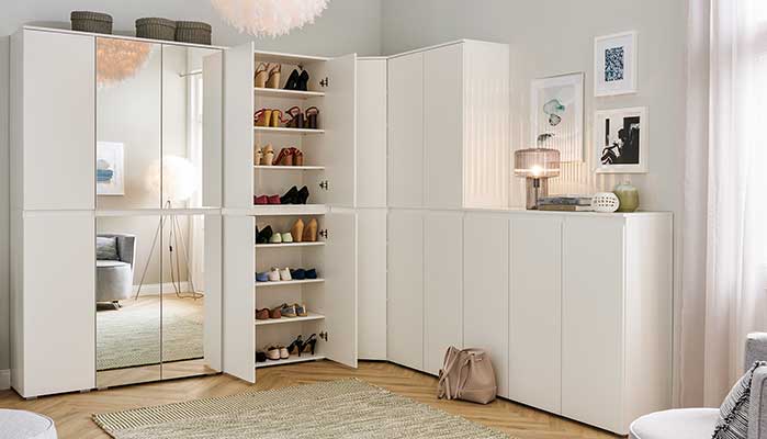Mehrere weiße hohe und halbhohe Schränke über Eck nebeneinander, zwei große Spiegelfronten,  zwei geöffnete Türen, die  Regalböden mit vielen Schuhen zeigen